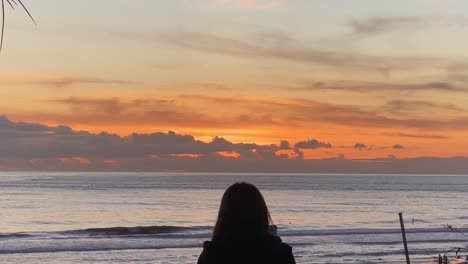 silhouette of woman recording video over carcavelos beach and surfers at the sunset background on the atlantic coast of portugal