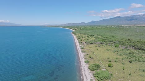 Drone-flight-over-sandy-beach-of-Ocoa-and-blue-Caribbean-Sea-with-green-scenery-at-summer