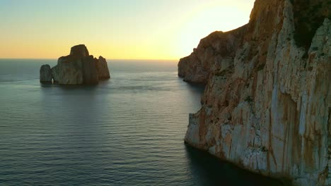 Panoramic-aerial-drone-orbital-shot-of-steep-cliff-near-Porto-Flavia,-Masua,-Province-of-South-Sardinia,-Italy-during-evening-time