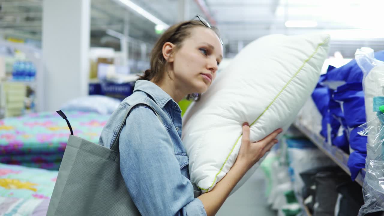 linda, positiva mujer caucásica en la tienda. concepto de compras. tomar una almohada suave del estante y poner su cabeza en. tomar una siesta, divertirse, sonriendo