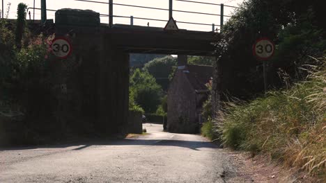 Quiet-Country-lane-on-a-sunny-day-with-Cars-in-the-distance,-Static-Wide-Shot