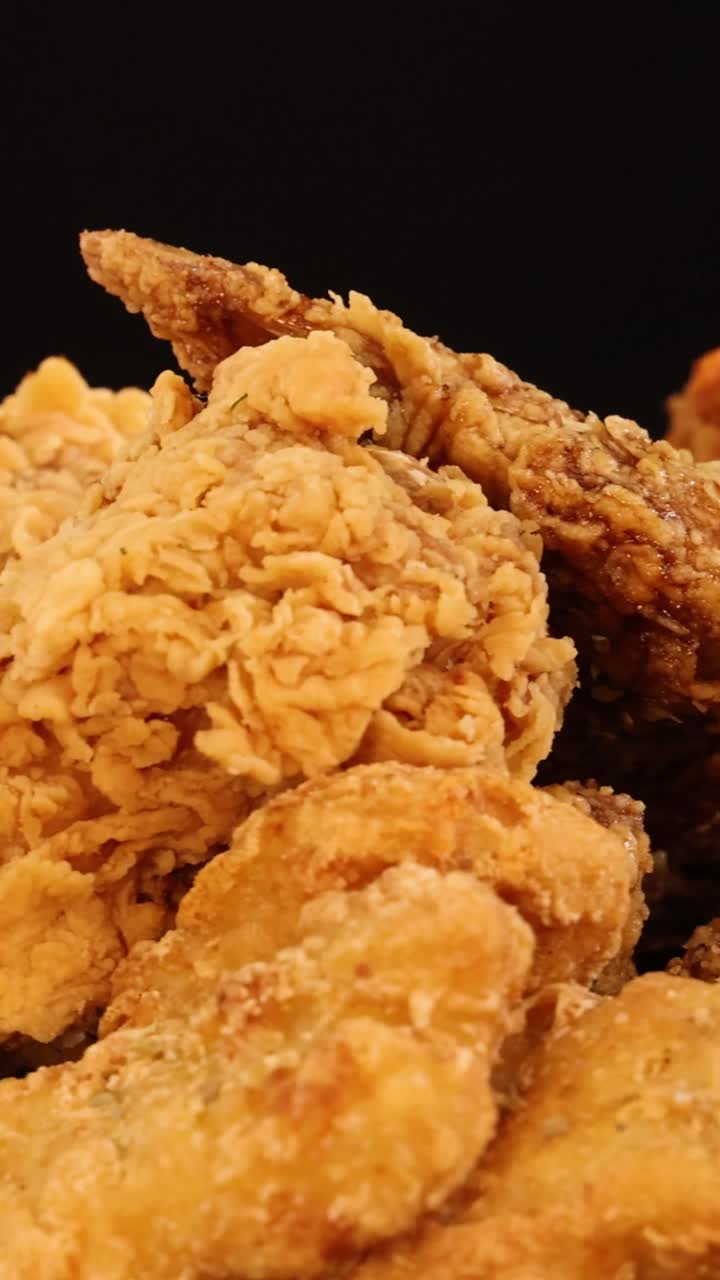 Una toma vertical cerrada de trozos de pollo frito dorado girando sobre un fondo negro.