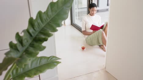 Mujer-Afroamericana-Sentada-En-La-Puerta,-Leyendo-Un-Libro-Y-Bebiendo-Té,-Cámara-Lenta