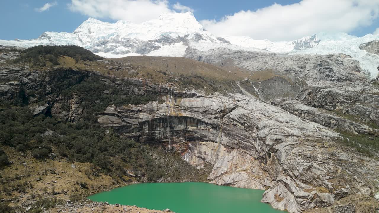 Aerial parallax shot of stunning turquoise Laguna 513 below snowy Hualcán Mountain in the Peruvian Andes, surrounded by dramatic rock and forest