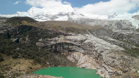 aerial parallax shot of stunning turquoise laguna 513 below snowy hualcán mountain in the peruvian andes, surrounded by dramatic rock and forest