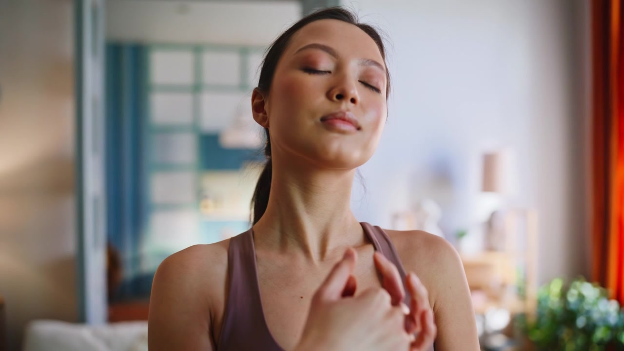 Mujer tranquila estirando las manos con los ojos cerrados en casa. Meditación, respiración, bienestar.