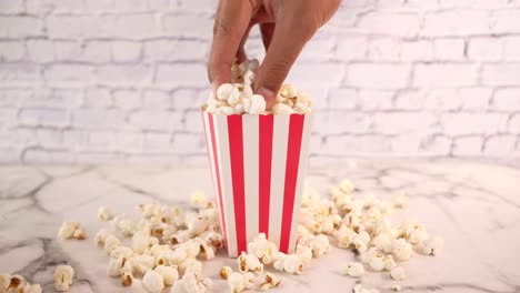 hand reaching for popcorn in a red and white striped box