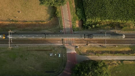 Crossing-railroad-tracks-with-a-highway-in-a-rural-area-of-the-united-states-with-a-train-passing-by,-top-down-shot