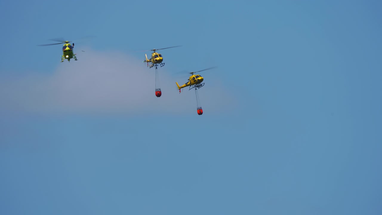 Gul brandbekämpningshelikopter med vattenbehållare mot blå himmel