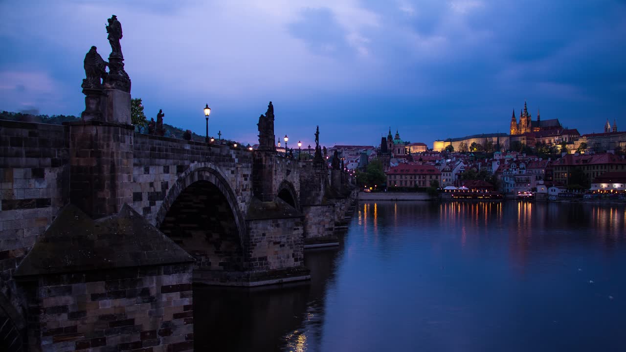 timelapse de día a noche desde praga, república checa desde al lado del puente carlos en el río vltava con vistas al castillo de praga mientras la ciudad se ilumina durante la noche