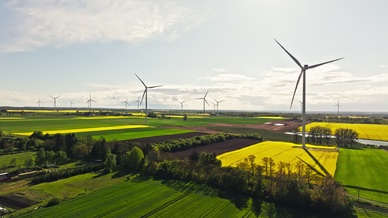 Wind Turbines On Vibrant Green And Yellow Fields. Sunny Rural Landscape. wide aerial shot