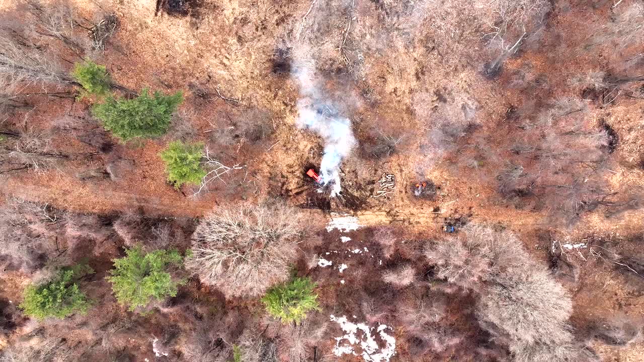 Kontrolleret afbrænding og røg i dvalende skovrydning med traktor i arbejde på en vinterdag. Luftfoto i fugleperspektiv.