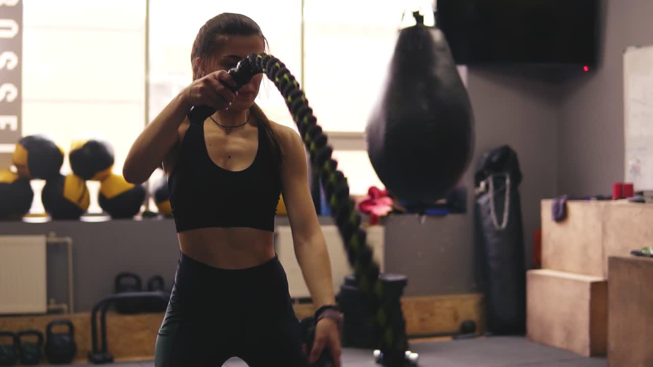 Physically strong brunette girl start the battle ropes workout at the gym.