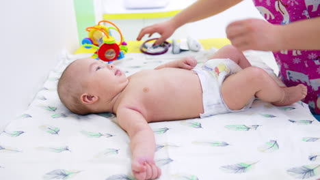 cute naked baby in diaper lying on the doctor's table. pediatrician standing in front of baby and kid watching the doctor curiously. side view.