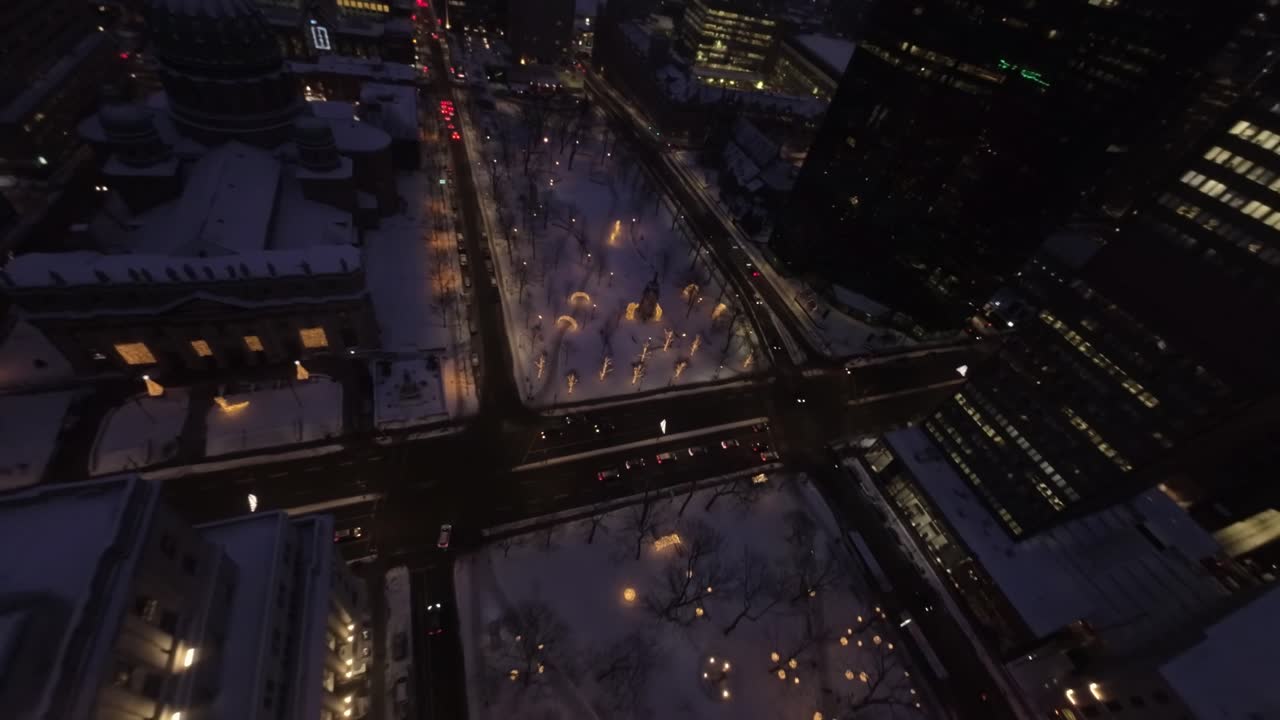 FPV drone pushes forward from rooftop of Sun Life building, descending smoothly to snowy streets of Square Dorchester, Montreal Downtown with stunning night views.