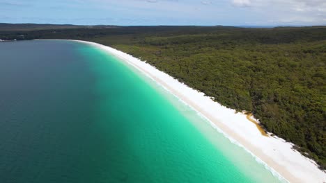 4K-drone-video-flying-backwards-to-reveal-more-of-the-stunning-Hyams-Beach,-a-long-stretch-of-white-sand-with-rainforest-on-one-side-and-blue-ocean-waters-on-the-other