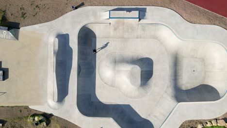 Die-Luftaufnahme-Aus-Der-Vogelperspektive-Fängt-Die-Dynamische-Bewegung-Eines-Skateboarders-In-Einem-Zeitlupenspektakel-Auf-Dem-Spielplatz-Des-Skateparks-Ein