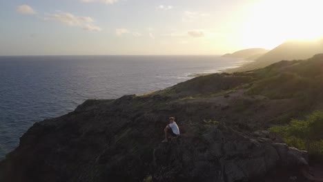 man resting on a rocky hill at sunset hiking in makapuu hawaii - aerial dolly pan