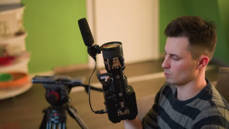 broadcast director adjusting camera lens, carefully working with camera equipment, including microphone and lights, preparing for filming or video production in home studio setting