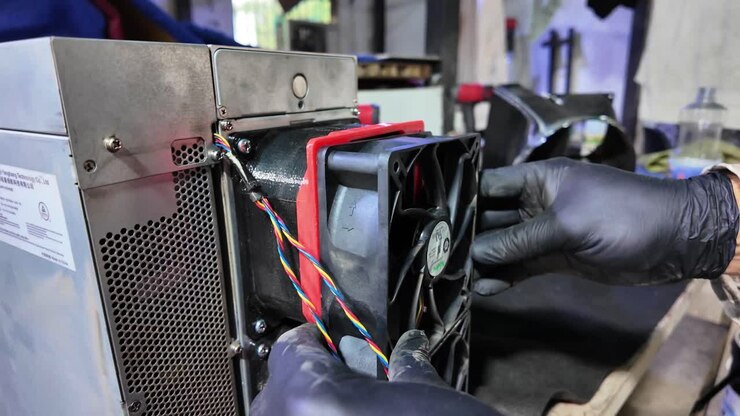 Close-up of a technician's hands in black gloves installing a powerful fan unit into a metal chassis for thermal management