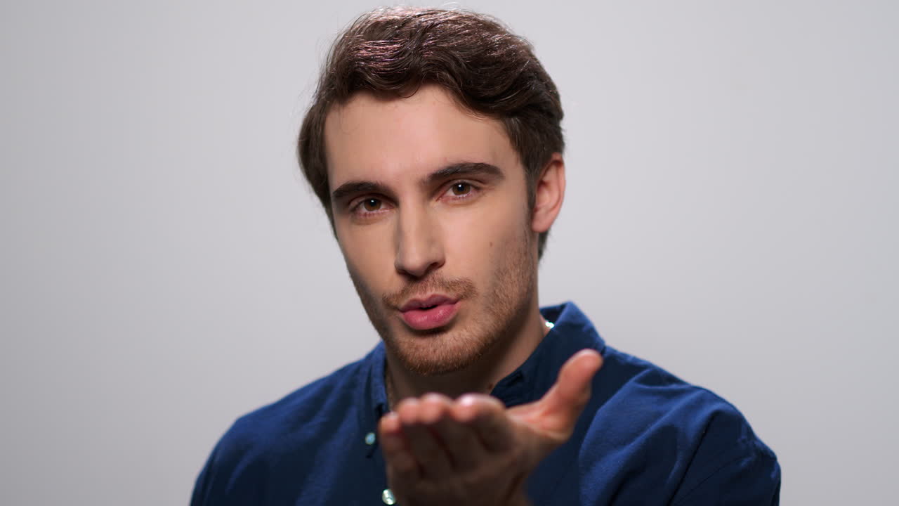 예쁜 남자가 카메라에 공기 키스를 보내고 있다. 미소 짓는 남자가 카메라와 유혹하고 있다.