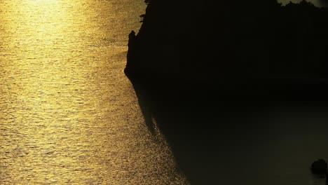 Tonos-Dorados-Del-Atardecer-Sobre-El-Mar-Jónico-Con-La-Silueta-De-La-Isla-De-Corfú,-Sombra-De-Barco-En-El-Agua