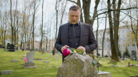 hombre de traje negro frente a una lápida con una rosa roja