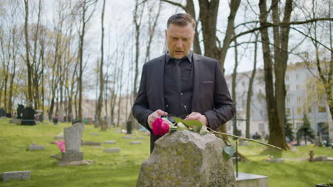 man in black suit in front a tombstone with a red rose