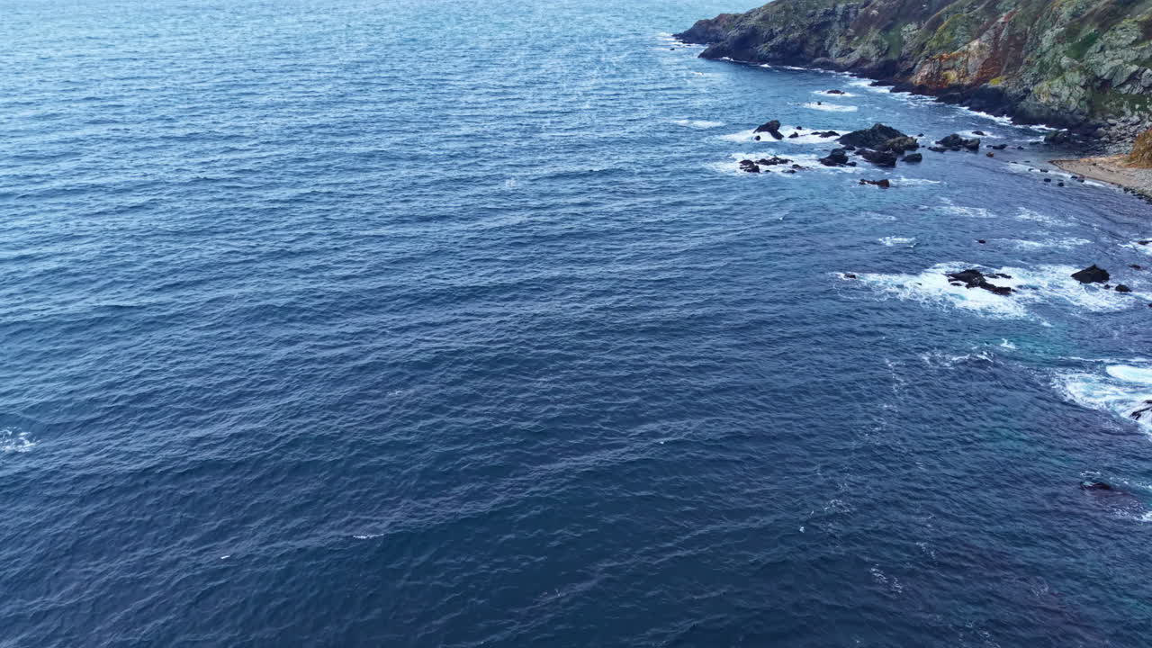 Deburan ombak laut yang dahsyat menghantam tebing berbatu saat fajar di dekat garis pantai yang tenang