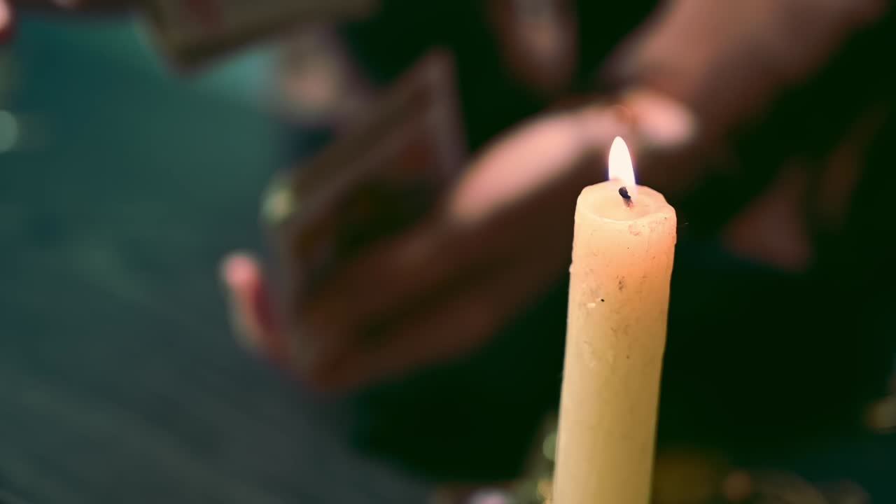 Fortune teller hands mix a card deck in background of a lit candle among mysterious esoteric jewelry. Overhead shot. Slow motion