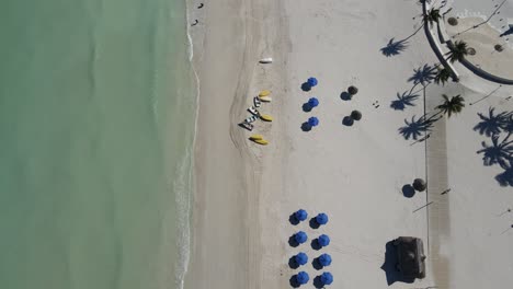 Beach-Drone-shot-turquoise-water-waves-white-sand-beach-chairs-vacation-sunny-paradise-palm-trees-and-beautiful-weather-for-relaxing