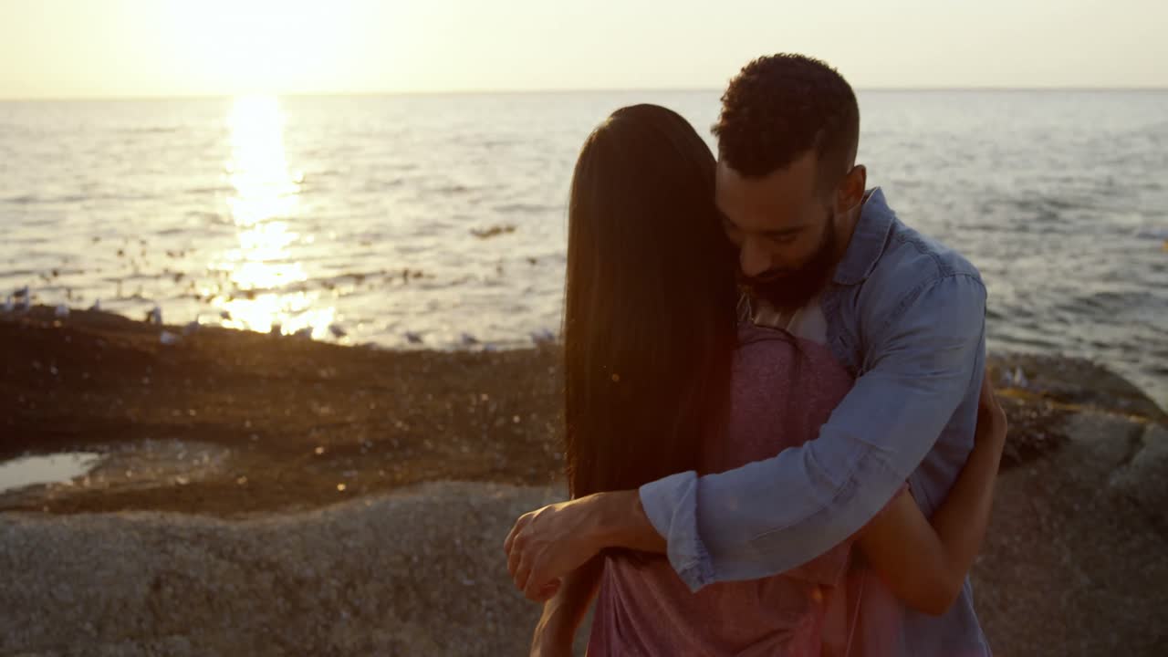 Giovane coppia romantica di etnia mista che si abbraccia in spiaggia 4K