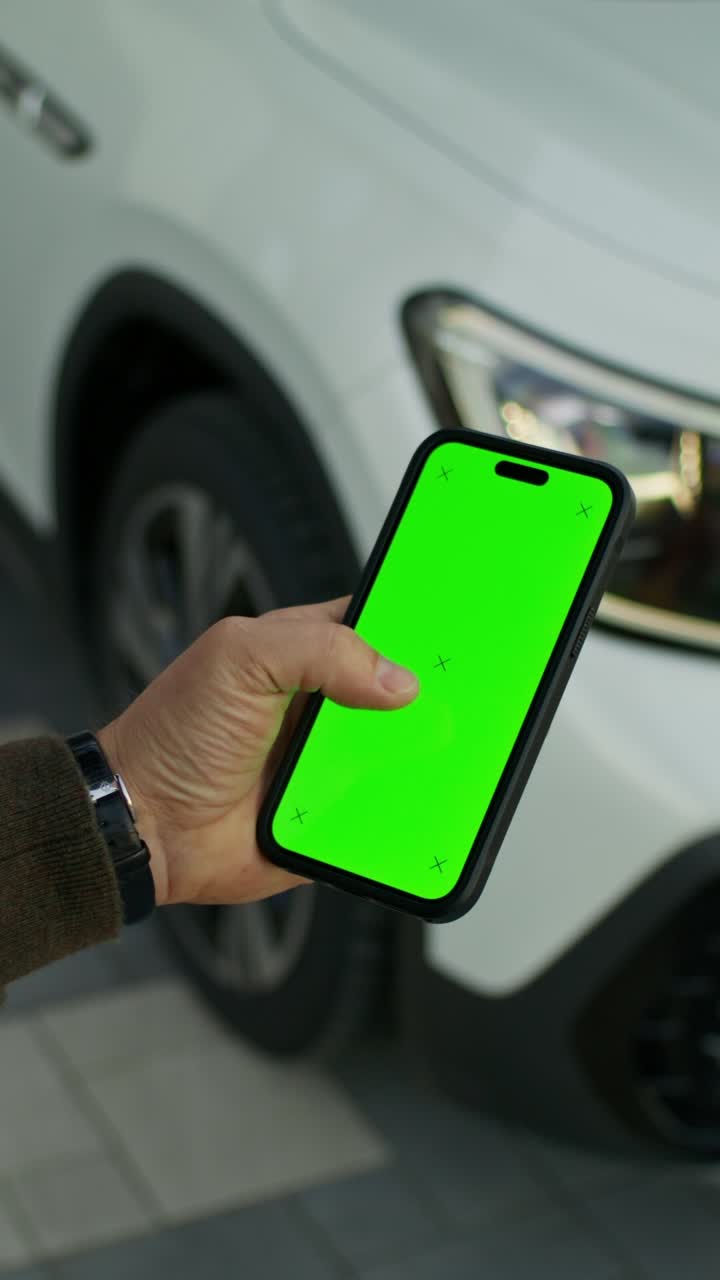 persona sosteniendo un teléfono inteligente con pantalla verde frente a un coche blanco