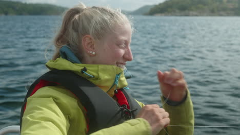 primer plano de una chica bonita pescando en un pequeño barco a motor en un hermoso fiordo en el sur de noruega, pesca amateur, chica sonriente con un chaleco salvavidas