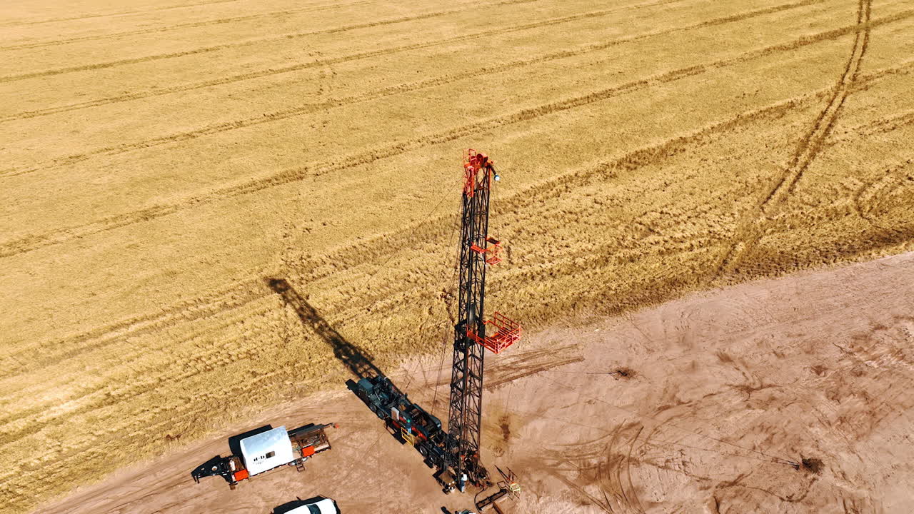 Top of the tower at the site for oil production. Ripe wheat field at backdrop. Drone footage above the drilling location.