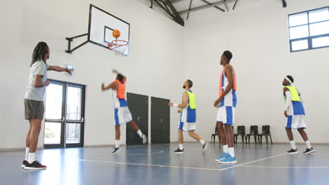 multiracial male basketball players passing basketball with coach giving instructions in gym