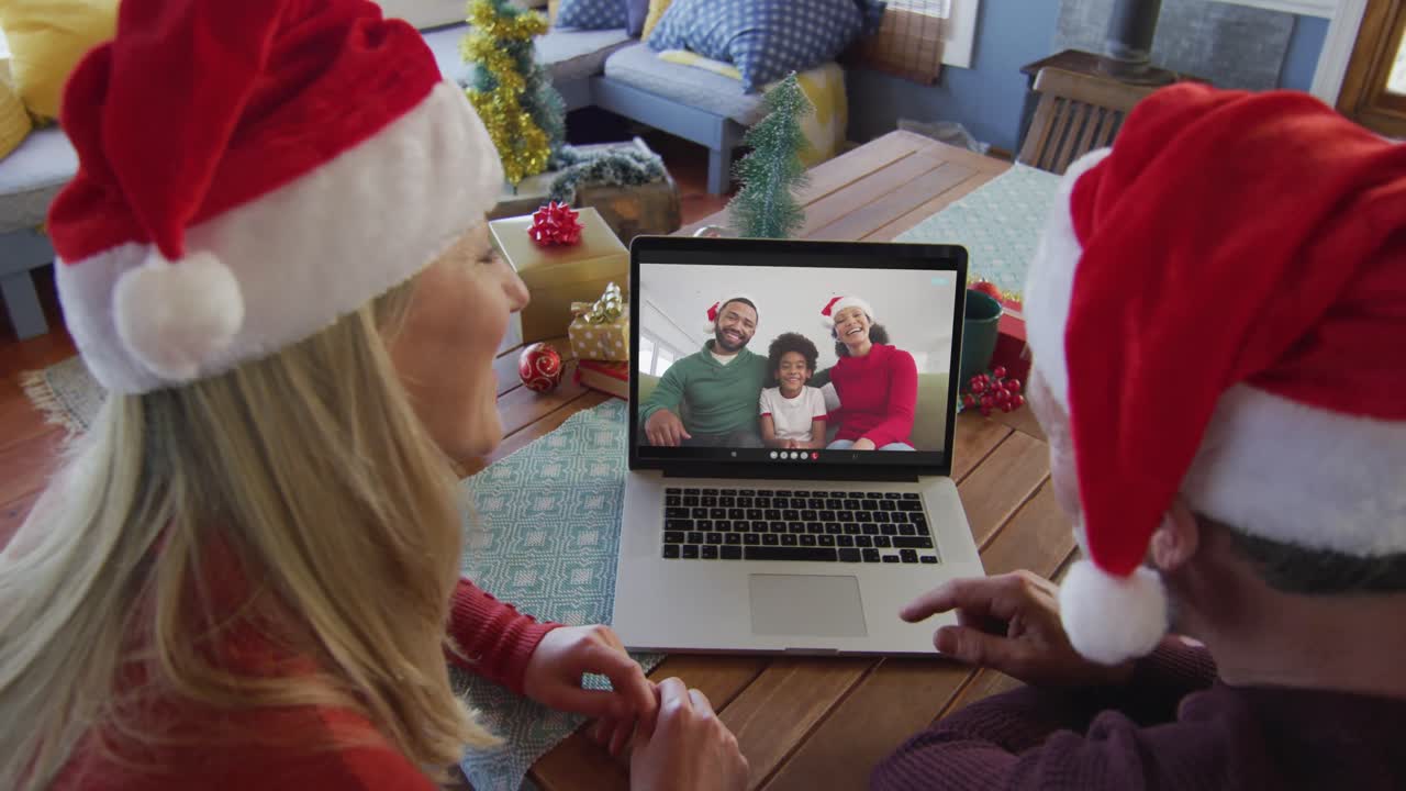 pareja caucásica con sombreros de santa usando una computadora portátil para una videollamada de navidad con la familia en la pantalla