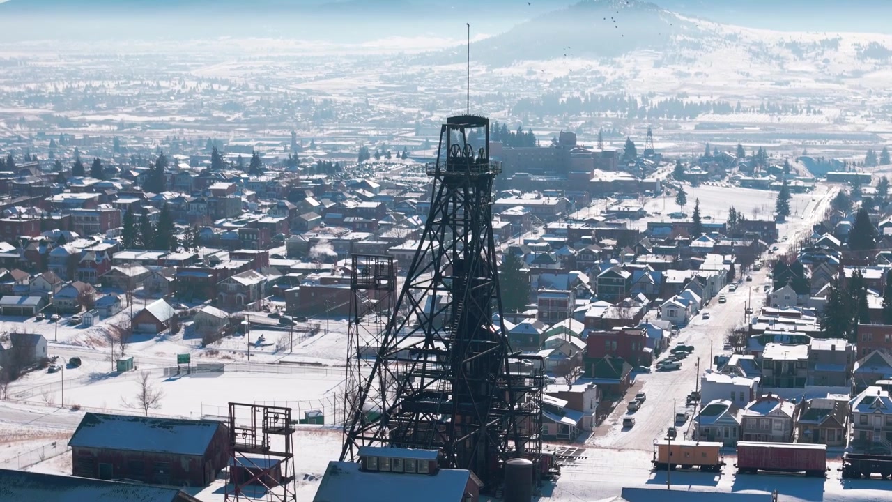Luftfoto fra drone om vinteren med fokus på vintage industrielle gruvetårn og snødekt historisk arkitektur i gruvesamfunnet Butte, Montana, under en vidstrakt horisont