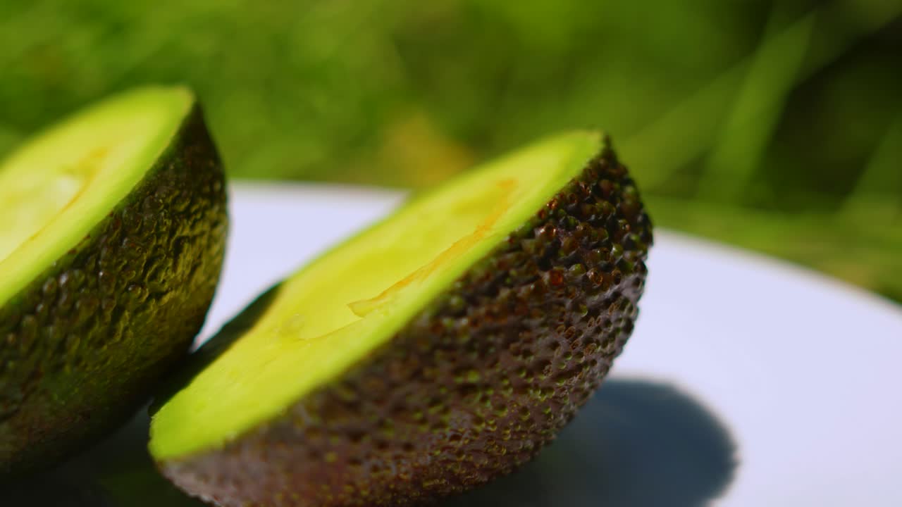 Close Up Details of Fresh Avocado Cut in Half on White Plate Under Natural Sunlight Outside. Healthy Organic Fruit Vegetable Food. Eaten at Breakfast or Used in Sauces