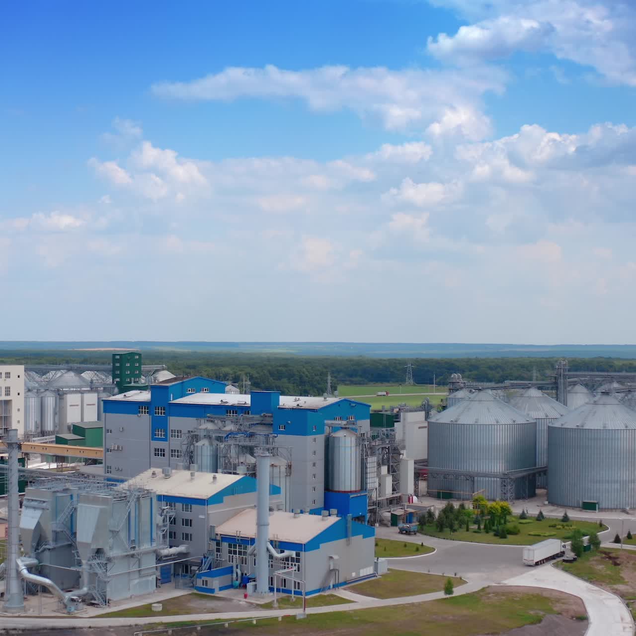 Modern plant on field. Metal silos with grain. Grain storage tank on green nature background. Grain storage on large factory. Aerial view