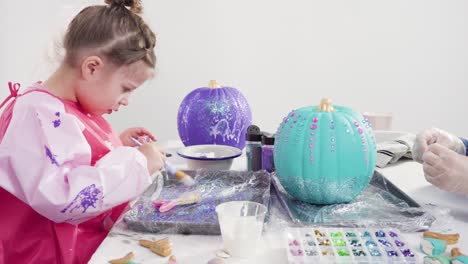 mother and daughter decorating art pumpkins with glitter
