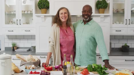 animation of happy diverse female and male senior friends preparing meal in kitchen, embracing
