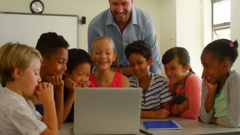 Adult-Caucasian-male-teacher-teaching-kids-on-laptop-in-classroom-at-school-4k