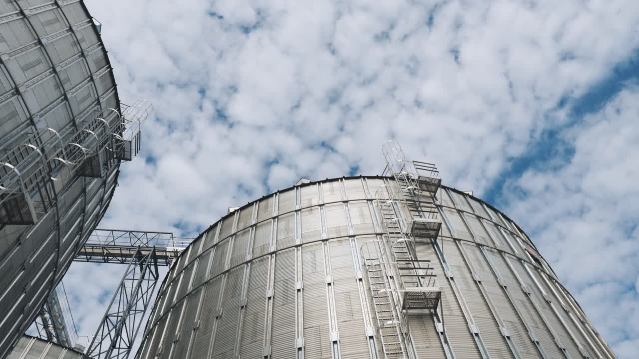 Top of large grain elevators. Silver agricultural containers under the moving sky. Metal tanks for storage crop in sunny day