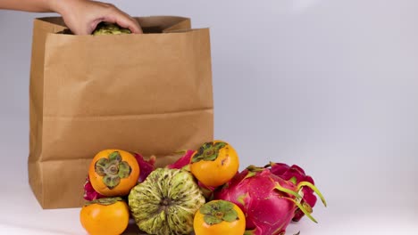 mano colocando varias frutas en una bolsa