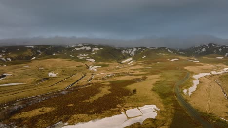 Aerial-landscape-view-through-a-mountain-valley,-covered-in-melting-snow,-in-Iceland