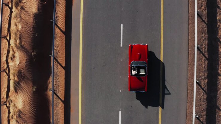 Ripresa dall'alto di un'auto cabriolet rossa che viaggia su una strada nel deserto sotto la luce del sole - aerea.