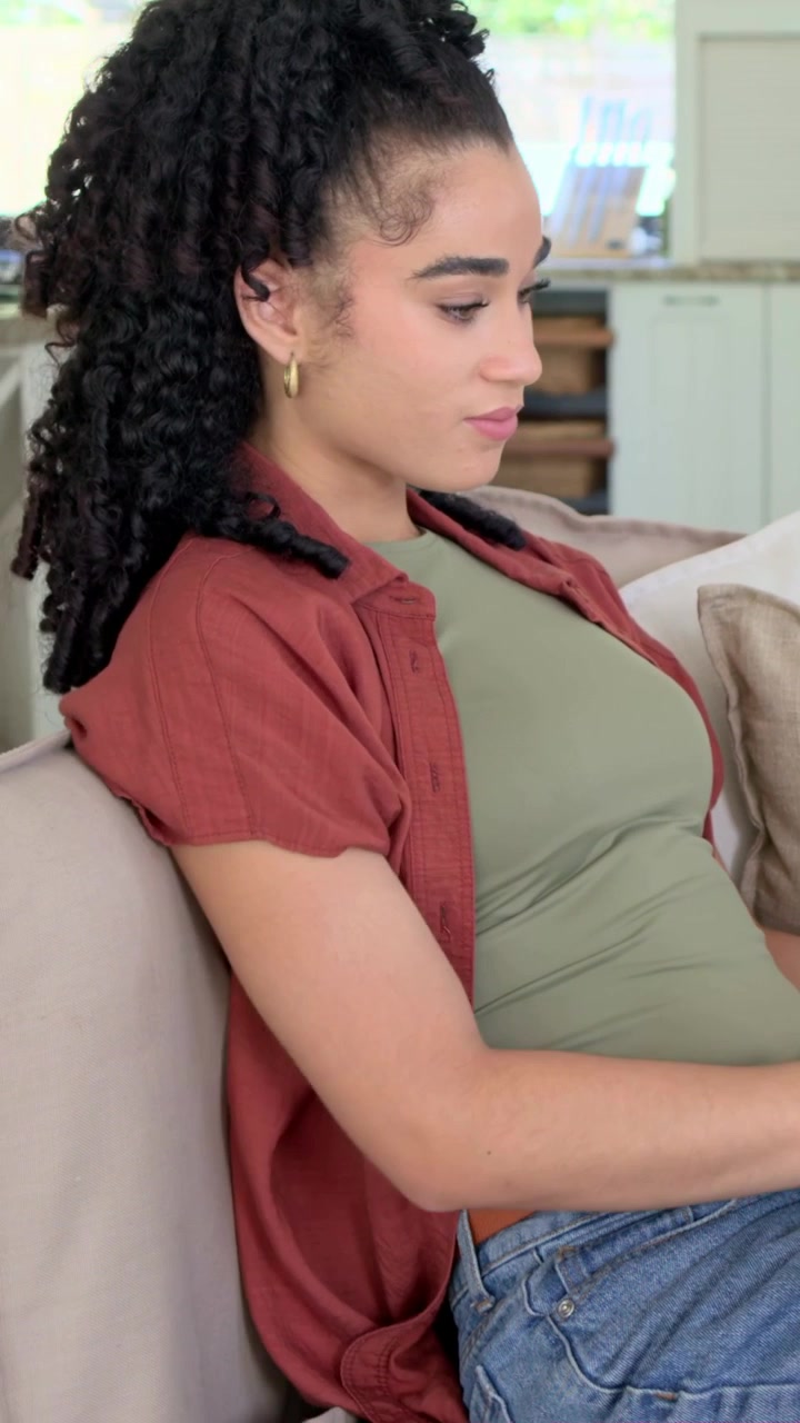 Vertical video: Glancing down, woman in green top and rust shirt typing on laptop on sofa, working