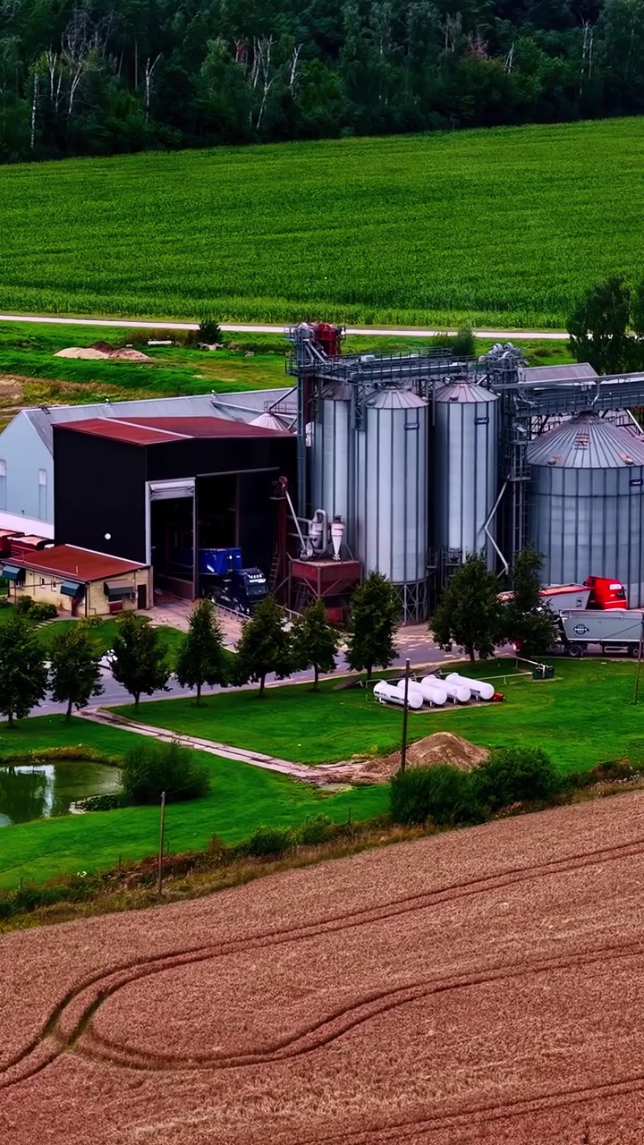 Een luchtfoto van een agrarische faciliteit met silo's en aangrenzende gebouwen, omringd door landbouwgrond.