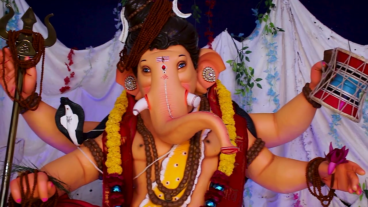 Primo piano del volto di un idolo di Ganesh vestito come il Signore Shiva che tiene un trishul e un damru, con segni tripund sulla fronte e ghirlande di calendula durante il festival di Ganesh Chaturthi in India